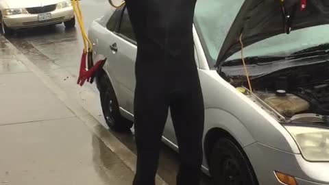 Man in wet suit jumpstarting car