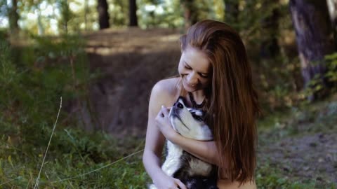 Pretty fair skinned young woman sitting on knees and hugging dog is happy pan