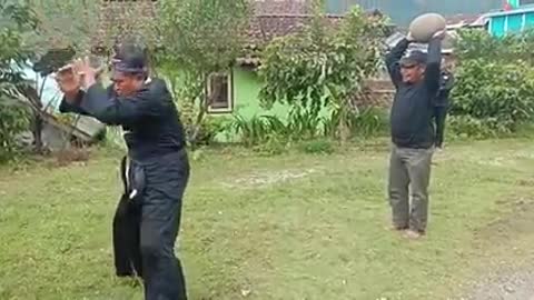 Chinese man testing how strong his back is by allowing another man to throw a rock into his back