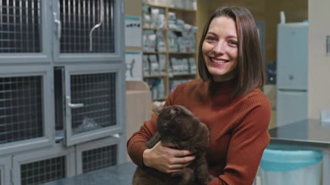 cat in arms petting it smiling to camera standing at veterinary clinic indoors