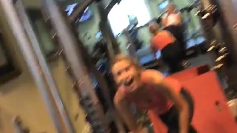 Girl in a pink top at a gym falls after lifting heavy weight