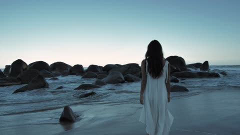 Woman walking on beach towards bouldersWoman walking on beach towards boulders