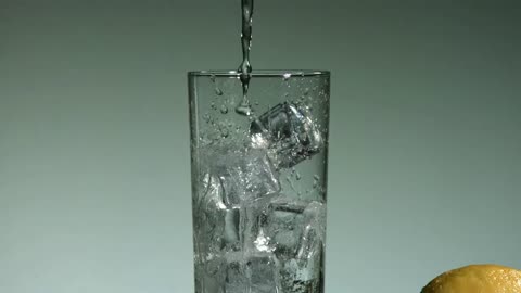 Water drops falling into a glass with ice cubes