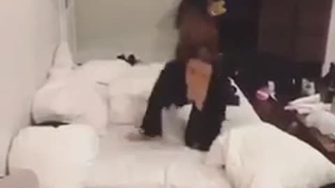 Black v neck girl does backflip on white bed and falls off