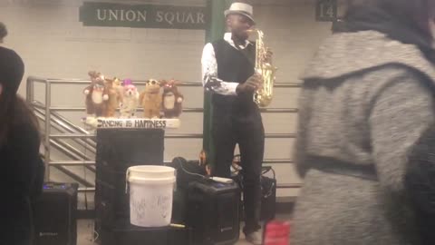 Musician in subway station playing saxophone, dancing puppets behind