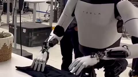 Tesla Optimus folds a shirt. Teslabot is not yet performing this action on its own.