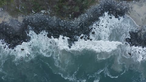 Top aerial shot of seashore with black shore rocks being hit by waves