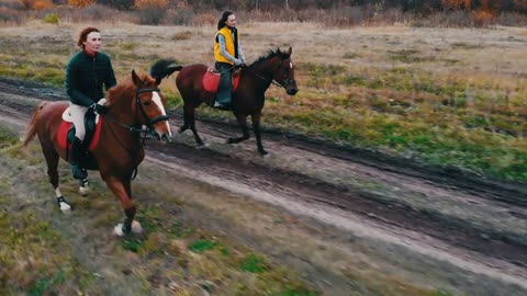 Two ginger horses with equestrians on their back are galloping on the road with puddles