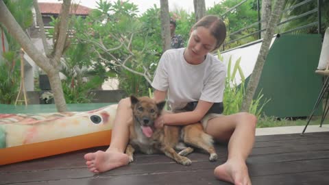 Joyful Caucasian girl wearing white T-shirt and shorts sitting outdoors petting her lovely dog