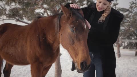 Pretty smiling woman strokes muzzle of adorable horse standing in winter ranch