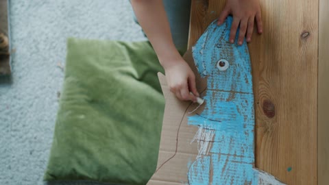 A Child Coloring a Cardboard Shark With Chalk