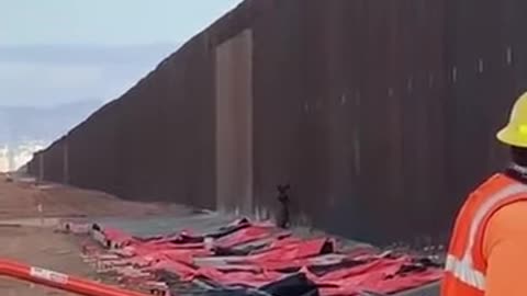 Man climbs the US-Mexico border while people are working on it