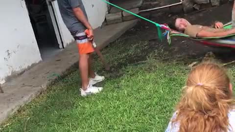 Guy pushes friend on hammock and then cuts rope with machete knife friend falls on ground