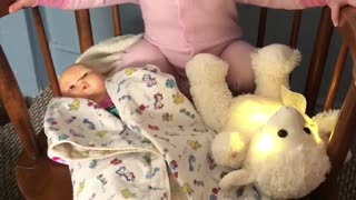 Tiny toddler rocks baby doll to sleep