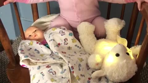 Tiny toddler rocks baby doll to sleep