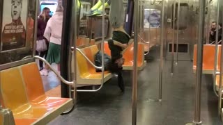 Guy in grey sweats hanging upside down on subway