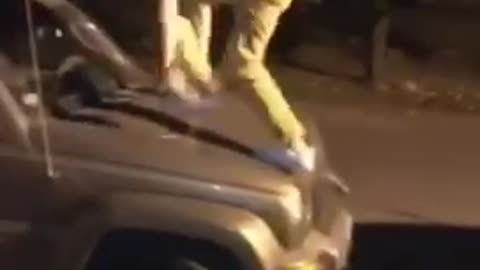 Guy jumps onto jeep and then falls onto black car and falls onto ground