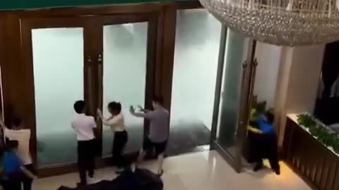 Hotel workers try to hold open doors hit by powerful gusts of wind from super typhoon.