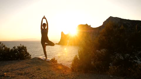 Woman doing yoga by the sea at sunset