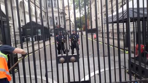 Armed officer police pushes a man out side Downing street. cleaners arrive to pick up tennis balls