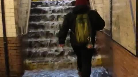 Person in red beanie walks up stairs with water running down