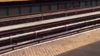 Man wearing a large feather hat, walks down the trains station with his bike