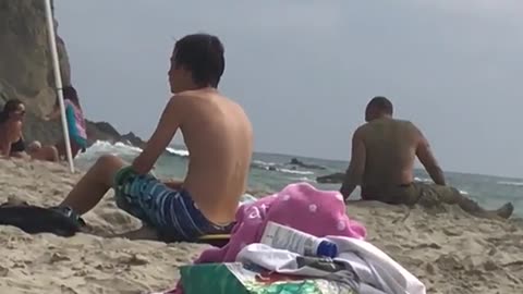 Old shirtless man puts stick in ear at beach plays with sand