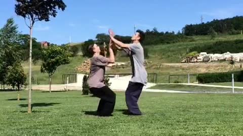 Two guys in grey shirts do back flips together