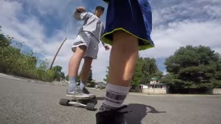 Guy on scooter kicking to speed up kicks friend on skateboard off