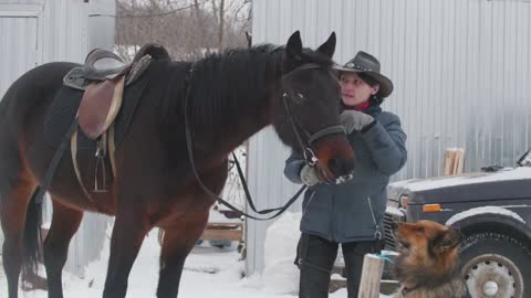 Woman in cowboy hat with horse and dog standing on snow field