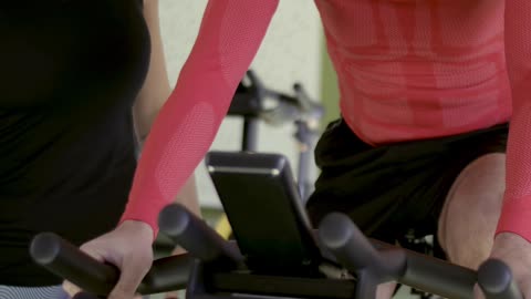 A Man Using a Stationary Bike while being Supervised by His Instructor