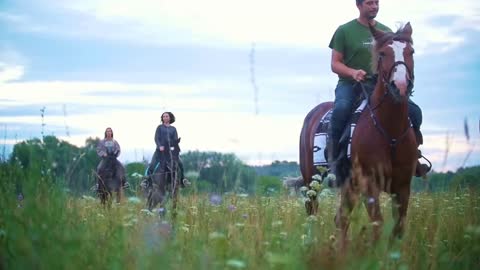 Group of young equestrian on horseback rides through the meadow with flowers