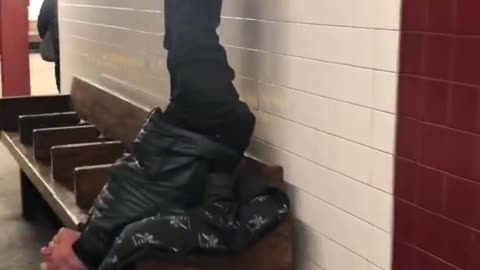 Man sits upside down on wooden bench with legs straight in the air