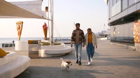 Cheerful young couple walking Jack Russel terrier dog outdoors near the sea