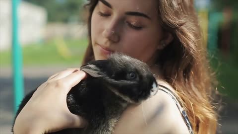 Young pretty woman stroking and kissing small fluffy rabbit in the garden in summer. Close-up