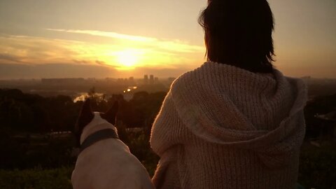 A woman with her dog watching the sunset