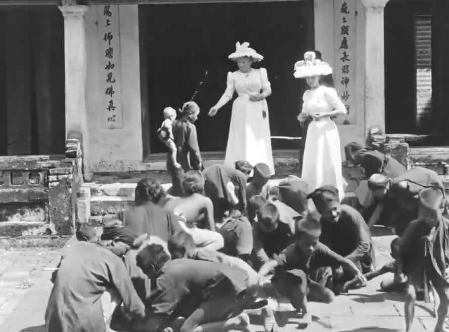 The wife of Paul Doumer and her daughter throwing coins at Vietnamese children, 1900