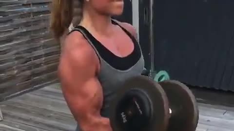 The girl performs lifting of dumbbells on biceps