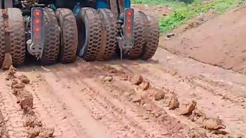 Container trucks loaded with heavy equipment pass through roads full of mud