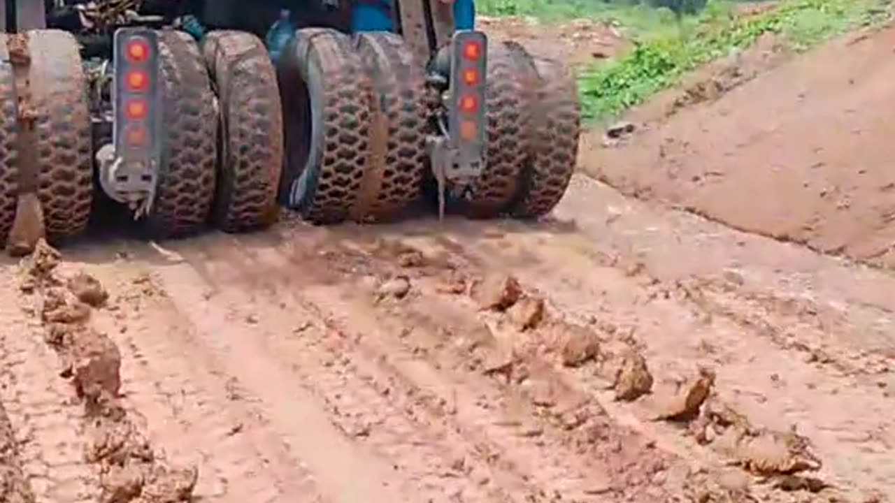 Container trucks loaded with heavy equipment pass through roads full of mud