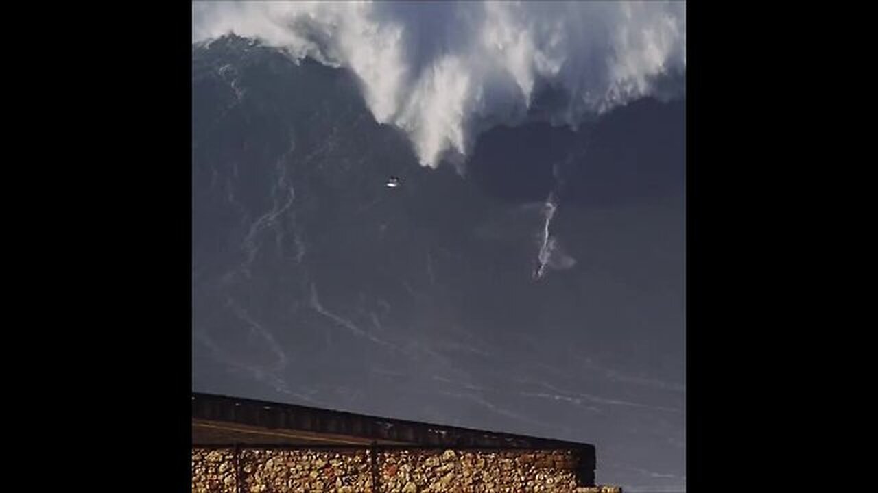 A surfer straddles a wave as high as a six-story house, Portugal.