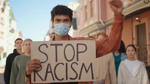 Young man wearing a face mask stands out in front of a group of friends in a city street.