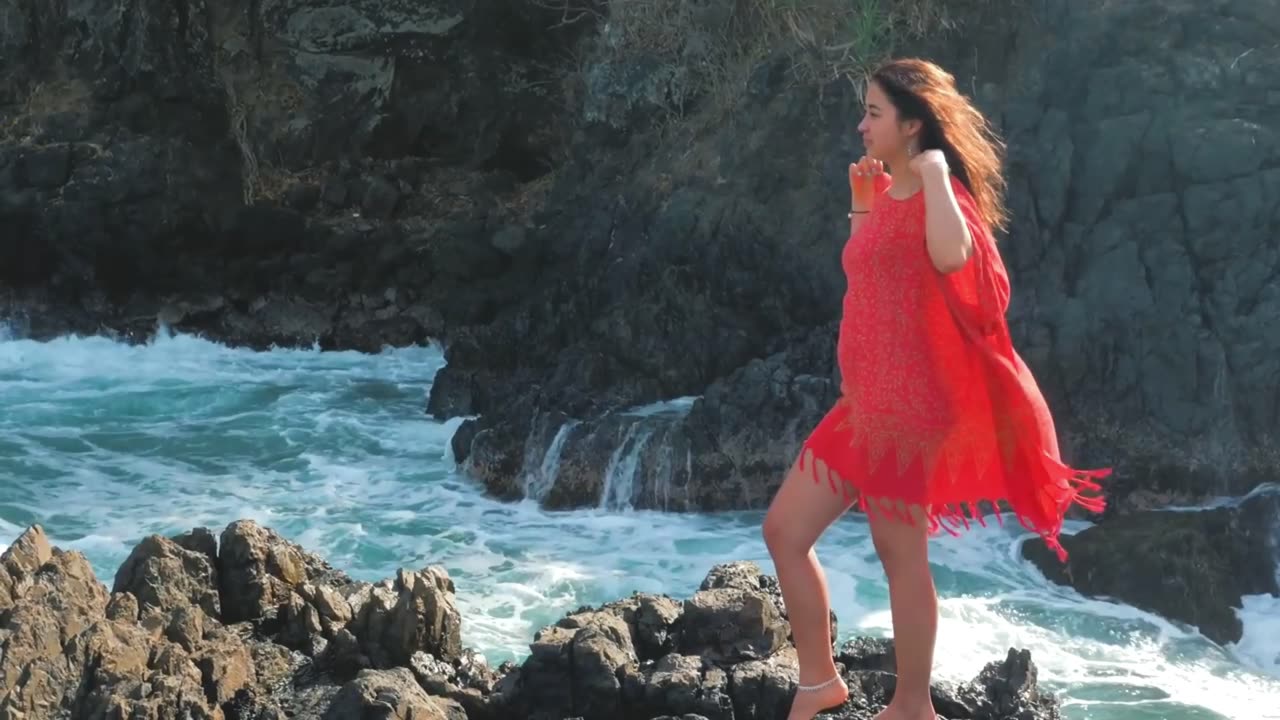 A beautiful woman with an attractive face wearing a red nightie looks out over the sea.