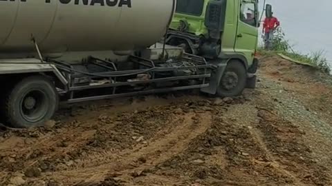 The tilted truck almost rolled over a muddy and uphill road