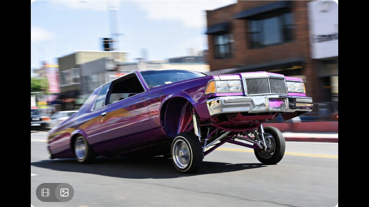 A photograph of a low rider car in motion, featuring lifted wheels and vibrant paint, against a blur