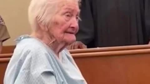 She's 91 years old, standing in a hospital gown, hands in chains