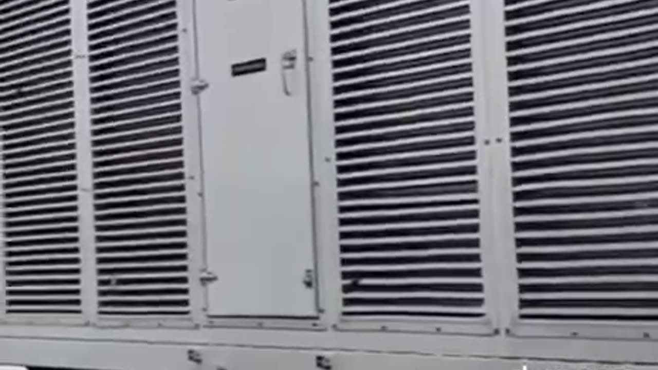 Man films a fleet of green Amazon electric vehicles charging by a massive diesel generator