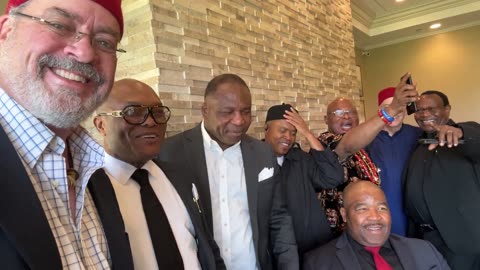Nigerian men in traditional attire and suits celebrating animatedly indoors, tagging President Trump