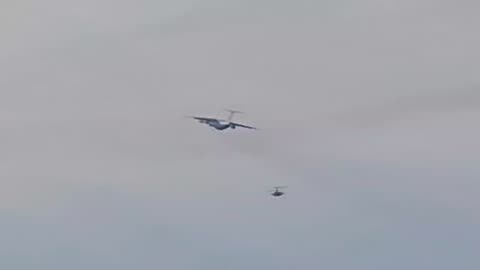 A Russian Air Force attack helicopter provides cover for a military transport aircraft.