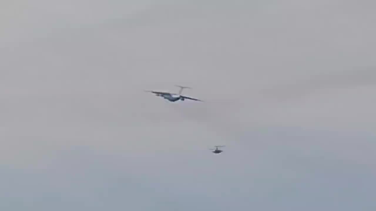 A Russian Air Force attack helicopter provides cover for a military transport aircraft.